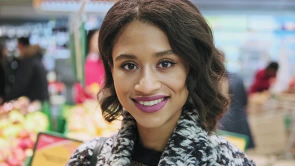 Beautiful Woman Looking at Camera and Smiling with Grocery at Background.