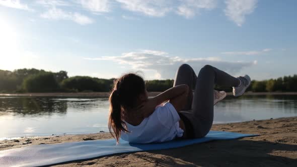 Woman Doing Sports Exercises, Shakes the Press at a Beautiful Sunset on the Beach, Sun Glare From