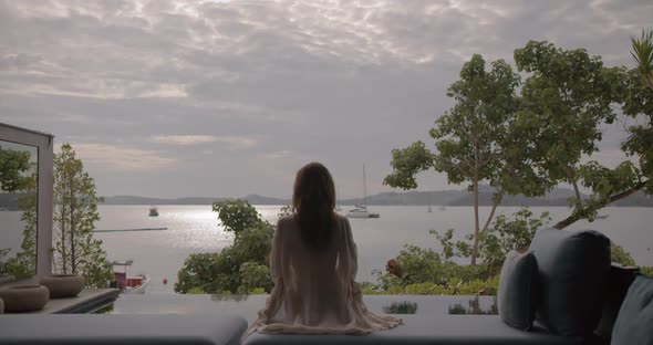 Backshot of Woman Sitting in Front of Swimming Pool and Looking to the Sunrise