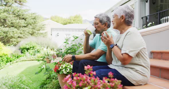 Video of relaxed biracial senior couple drinking coffee in garden