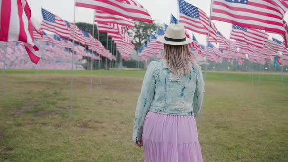 Woman Walking Between Waving American Flags in Park