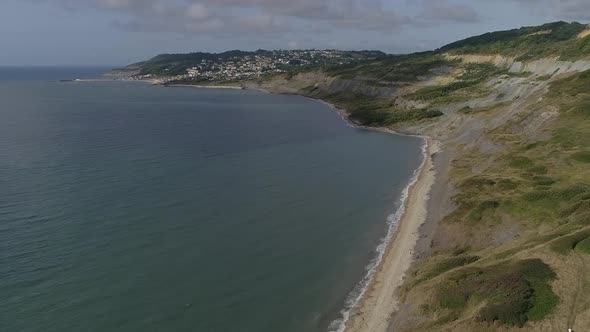 Aerial on the edge of Charmouth tracking forwards along the coast towards Lyme Regis. Glorious Juras