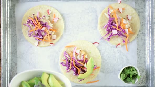 Preparing fresh fish tacos with cod and purple cabbage on a white corn tortillas.