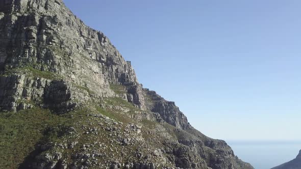 Aerial drone flight along Table Mountain rocks and epic reveal of Lion's Head in far background agai