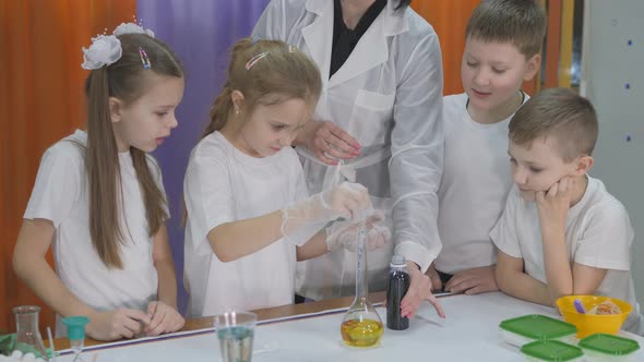 Chemical Experiments for Children. Girl Pours a Blue Liquid Into a Flask with a Yellow Liquid. Room