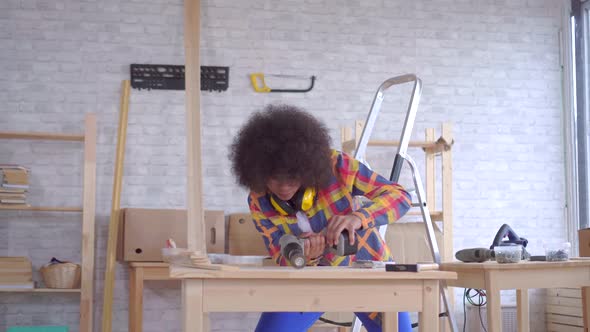 African Woman with an Afro Hairstyle Works on Wood in the Workshop