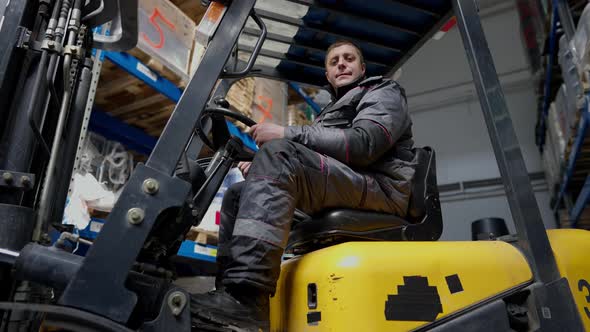 Wide Shot Side View of Smiling Confident Man in Uniform Sitting in Forklift Looking at Camera