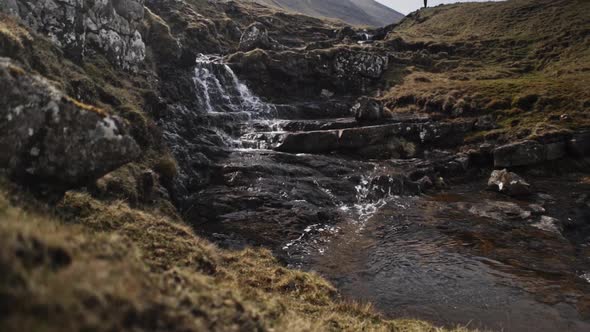 Tilting Upward Shot From Water Stream To Man Standing By Cliff in European Land