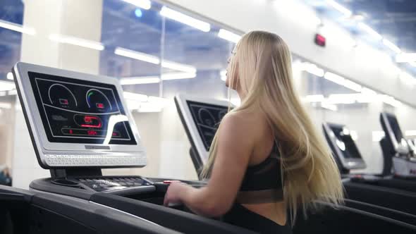 Young Attractive Caucasian Woman with Blond Hair in Black Sport Outfit Running on Treadmil at the