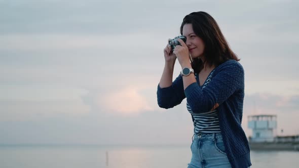 Young Woman Takes Pictures on a Vintage Camera By the Ocean. Portrait of a Girl with a Retro Camera