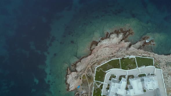 Aerial view of large white villas with garden in front at seaside in Greece.