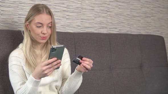 Young woman customer holding credit card and smartphone, buying from home.