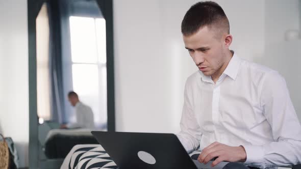 Serious Man Is Sitting on Bed and Printing Online Using Laptop at Bedroom