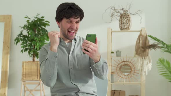 Man Sits at a Table Triumphantly Wins an Online Lottery on a Mobile Phone Reads Good Unexpected News