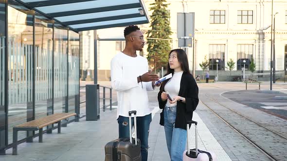 African Amercian Talking with His Joyful Asian Female Friend while they Waiting on Public Transport