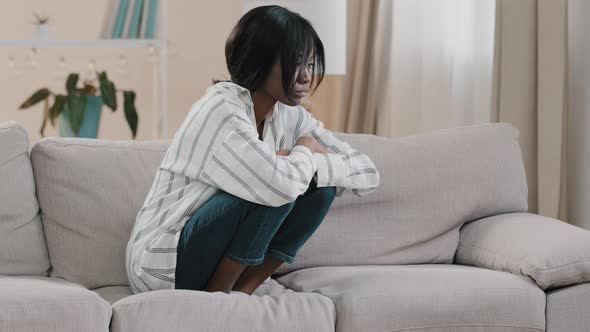 Young Tense Depressed Sad Woman Sitting on Sofa Hugging Knees Thinking About Personal Problems