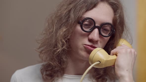 Headshot of Furious Young Man in Vintage Eyeglasses Yelling in Retro Telephone Handset and Hanging