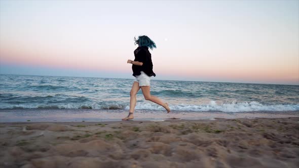 Pretty Woman with Blue Hair Runs Near Sea at Sunrise or Dawn, Enjoying Freedom During Summer