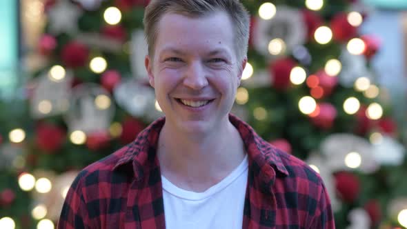 Happy Young Handsome Man Against Illuminated Christmas Trees Outdoors