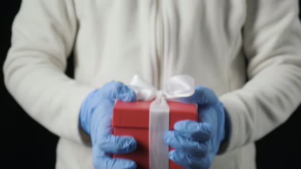 Little Girl's Hands in Blue Protective Gloves Giving Gift Box with White Ribbon