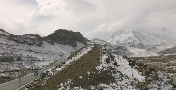 Aerial Rising Beside Empty Road To Reveal Snow Covered Mountain In Background At Hunza Valley