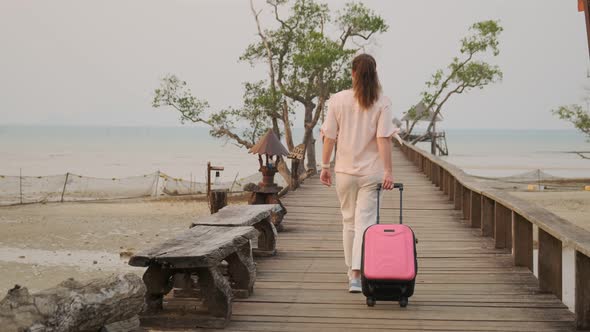 girl with suitcase goes on wooden pier to boat