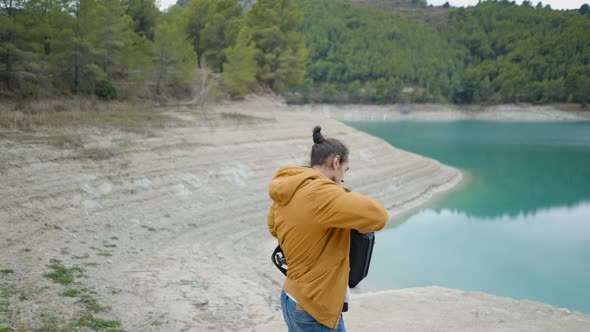 Young Man Takes Camera Out of Backpack and Photographs Lake in Spain