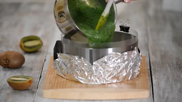 Pastry chef making a kiwi mousse cake on kitchen. Pouring kiwi jelly on top the cake.	