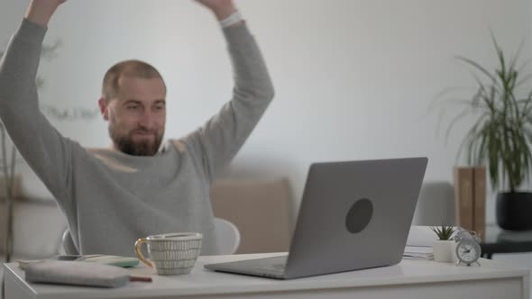 Happy man freelancer  with beard in a gray jacket relaxing at home  with a laptop