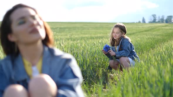 Blurred Portrait of Mother Daughter Playing with Plucked Flowers in Tall Green Grass