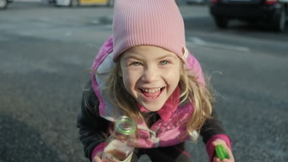 Funny little girl in a pink hat and waistcoat laughs and looks into the camera outdoor