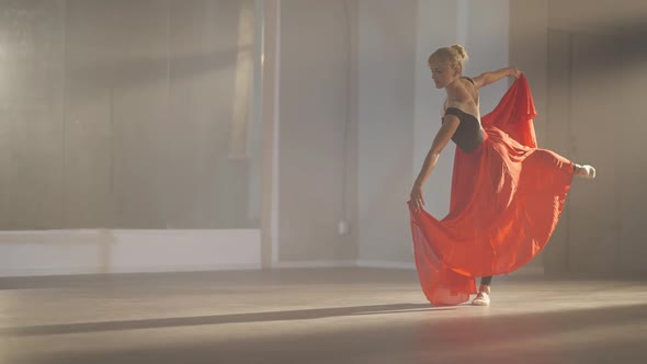 Wide Shot of Slim Professional Ballerina in Arabesque Ballet Position Holding Scarlet Red Skirt