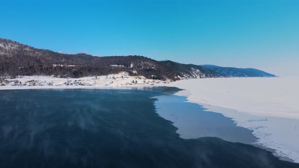 The river is split in half by ice. Vapour rises over the water. Drone footage