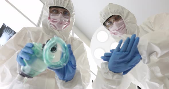 Two Doctors in Protective Suits and Masks Holding Oxygen Mask and Planning to Have Heart Massage