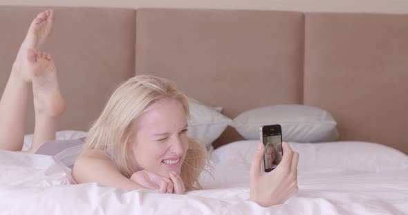 Woman lying on bed and taking selfie with smart phone in bedroom