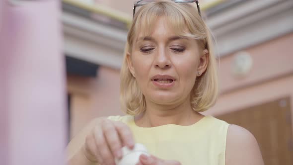 Close-up of Satisfied Blond Woman Smelling Moisturizer on City Street Outdoors. Portrait of