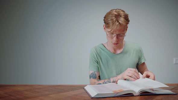 Guy in Glasses Studying and Stressing Reading a Textbook in Empty Grey Room