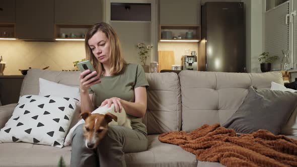 Woman Sitting on Sofa with Dog and Use Smartphone