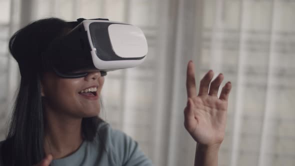 Happy Asian girl using 3D virtual reality headset at home.