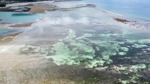 Aerial drone over a solo traditional fishing canoe boat at low tide with sand bars, coral reefs and