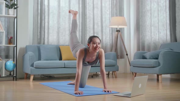 Asian Athletic Female Exercising, Stretching And Practicing Yoga At Home With Online Coach In Laptop
