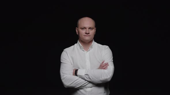 An elegant bald man stares in front and poses for the camera on a black background