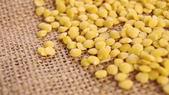 Uncooked lentils on a rustic rough burlap. Raw yellow split legumes. Macro