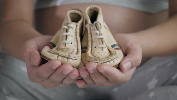 Pregnant Woman Shows Her Hands Nice Small Shoes For A Baby Close Up