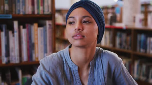 Asian female student wearing a blue hijab thinking and learning her chin on her hand