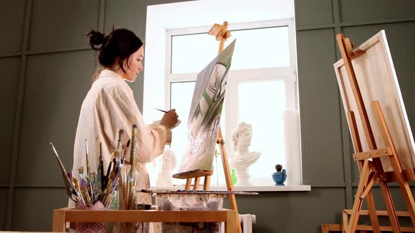 Art Studio  Young Woman in Stained White Shirt Changing Brushes and Drawing a Painting