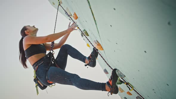 Young Woman Hanging on Outdoor Rocky Wall Looking for Right Way Up Below View