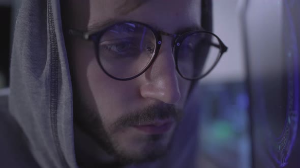 Close-up of Bearded Young Man in Eyeglasses and Hood Indoors. Male Caucasian Hacker or Programmer