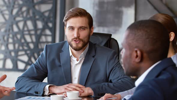 Smiling businessman in a suit listening to a colleague at a meeting with a team