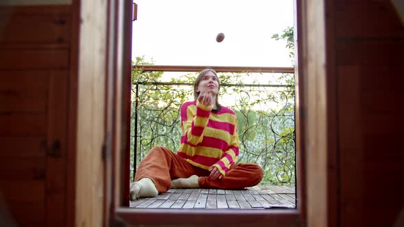Woman Sits on Her Balcony in Sweater and Juggles Fruit in Her Spare Time